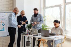 Diverse group of professionals in a bright, modern office gathered around a table, actively collaborating on a real estate...
